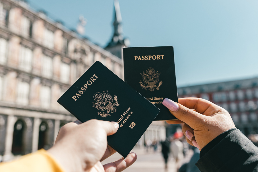 Two people holding out passports from the united states of America with a historical building in the background
