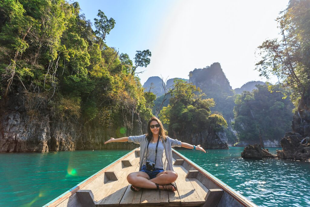 Tourist traveling woman sitting with open arms and a camera on a boat in a scenic location with beautiful islands behind her.