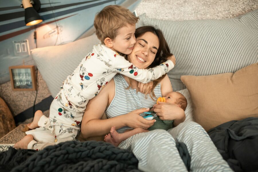 A mother holds a newborn while getting a hug from her toddler