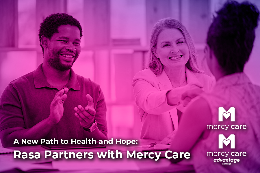 A smiling woman in a light blazer shakes hands with another woman across a desk, while a man next to them claps and smiles. The image has a pink overlay. Text on the image reads: “A New Path to Health and Hope: Rasa Partners with Mercy Care.” Mercy Care and Mercy Care Advantage logos appear in the bottom right corner.